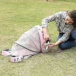 Femme en plaid interagissant avec un animal dans un transporteur rose, en pleine nature.