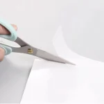 Ciseaux mint ergonomiques en train de couper du papier blanc lisse sur une surface claire.