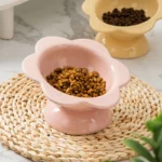 Bols alimentaires en forme de fleur rose et jaune sur un tapis naturel, décor chic pour animaux.