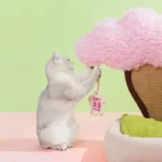 Un chat blanc curieux interagit avec un arbre en coton rose, évoquant la magie des fêtes.