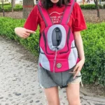 Jeune femme en t-shirt rouge avec porte-bébé coloré dans un parc verdoyant.