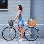 Jeune femme joyeuse sur vélo blanc avec chat dans un panier en osier.