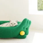 Lit pour chat en forme de main verte avec un chat blanc confortable.