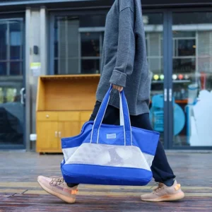 Personne décontractée avec un tote bleu, sweatshirt gris et sneakers, dans un environnement urbain.