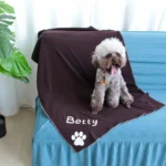 Un chien fluffy souriant sur un canapé bleu avec une couverture personnalisée Betty.