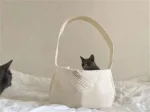 Sac tissé et chat curieux sur un lit blanc, moment de douceur et de complicité.