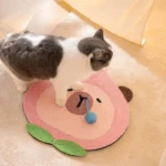 Un chat noir et blanc joue sur un tapis pour chat en forme de pêche rose.