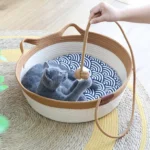 Un chat bleu allongé dans un panier chat en rotin avec un coussin à motif de vagues.